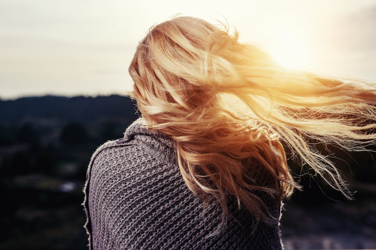 Back view of a woman with blonde hair blowing in the wind during sunset outdoors.