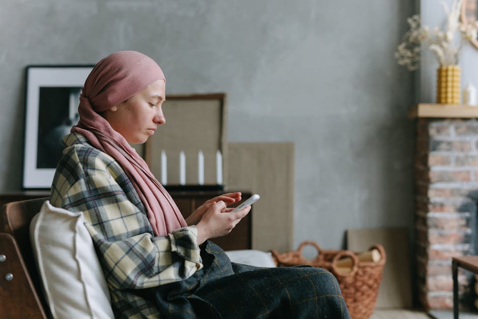 Kobieta w różowym hijabie siedzi na krześle, trzymając telefon w dłoniach. W tle widać nowoczesne wnętrze z elementami dekoracyjnymi, takimi jak świeczniki i kosze.